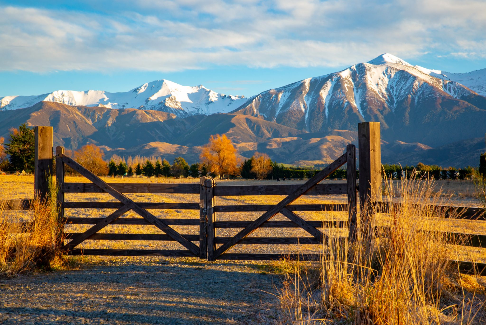 Picturesque snowy mountains behind a wooden farm gate.