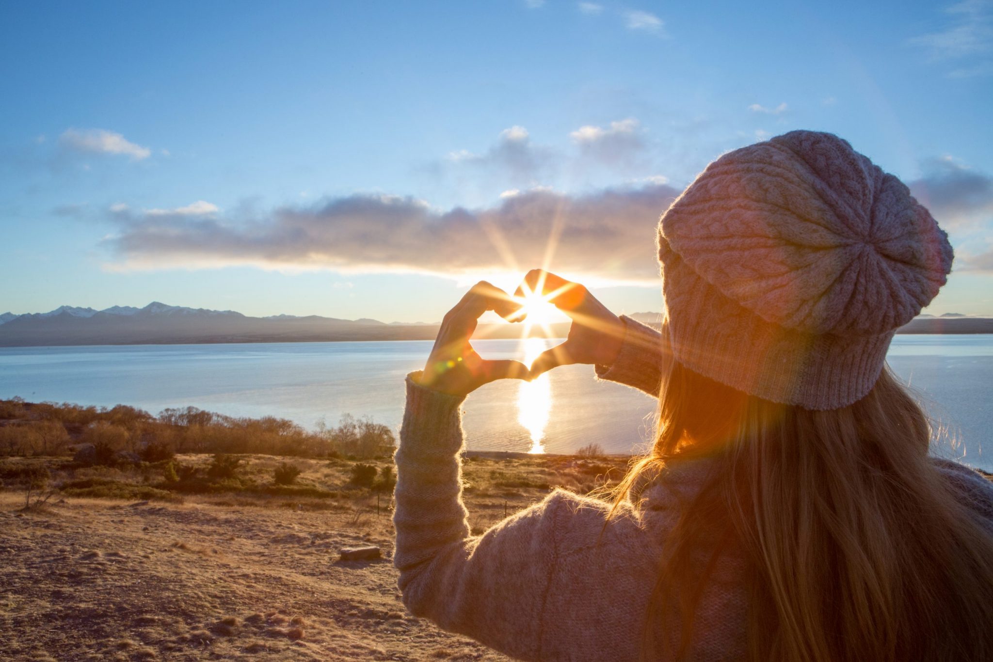 Young woman framing sunrise into heart shape finger frame